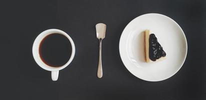 Top view of blueberry cheese cake, black of coffee and tea spoon on black background in vintage tone. Flat lay of Hot drinking and desert food on table. Group of white dishware. photo