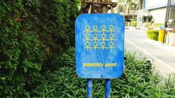 Blue assembly point sign for emergency case such as fire, earthquake, disaster with green tree and access, entrance or automatic door entry and exit background. Incident and Information for people. photo