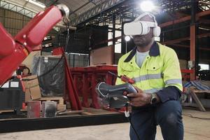 An African American engineer with VR glasses controls robotic arm, virtual simulator software in mechanical manufacturing factory, and intelligent automatic machines technology in industry innovation. photo