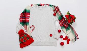 cierre el espacio de copia de sudadera de plantilla en blanco gris. concepto de vacaciones de navidad. sudadera con capucha de maqueta de vista superior, bufanda, sombrero. decoraciones navideñas rojas sobre fondo blanco. feliz año nuevo accesorios. traje de navidad foto