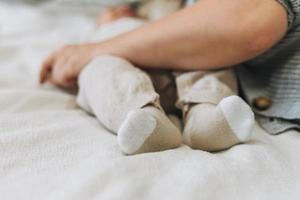 lindos pies de bebé en calcetines beige, niño con madre en la cama, maternidad feliz foto