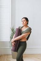 Attractive middle aged brunette woman in sportswear with yoga mat in light studio photo