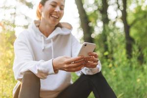 Young slim woman brunette in sport clothes running and using mobile phone at autumn park on golden hour sunrise time. Health and wellness, fitness lifestyle photo