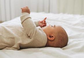 Cute smiling baby boy in beige overall 5-6 month on bed natural tones photo