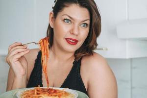 Beautiful happy sensual brunette young woman plus size body positive with dish of spaghetti enjoying her life at the home photo