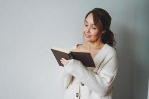 Atractiva y amable mujer morena sonriente de mediana edad leyendo un libro en casa vibraciones acogedoras temporada de frío foto