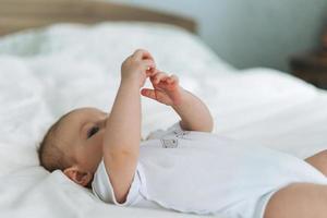 linda niña de 2 a 4 meses en la cama con sábanas blancas, enfoque selectivo de tonos naturales foto