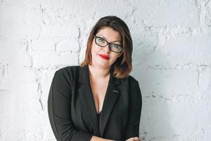 Beautiful smiling young woman business lady in glasses and black jacket against white wall photo