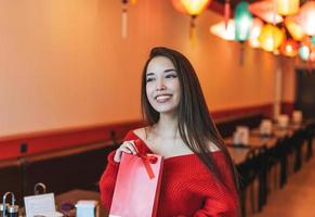 Beautiful young asian woman in red clothes with red gift bag in restaurant, celebrating Chinese New Year photo