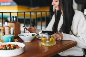 Attractive young brunette smiling woman in casual using mobile phone having brunch in the cafe photo