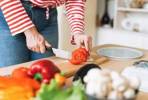 Fresh vegetables green salad, peppers, mushrooms and eggplant on kitchen table. Young woman plus size body positive in red longsleeve cooking using book with recipes on the kitchen photo