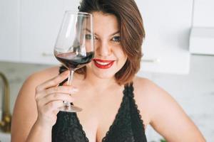 Beautiful happy sensual brunette young woman plus size body positive with glass of red wine enjoying her life at home photo