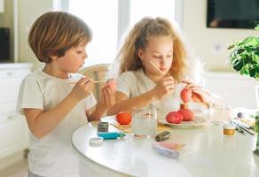 Two siblings brother and sister toddler boy tween girl painting easter eggs on kitchen at home on the spring sunny day photo