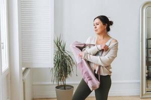 Attractive middle aged brunette woman in sportswear with yoga mat in light studio photo