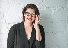 hermosa mujer joven y sonriente mujer de negocios con gafas y chaqueta negra contra una pared blanca foto