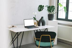 Modern workplace with an open laptop with white screen and green monstera on the marble table, mock up, template photo