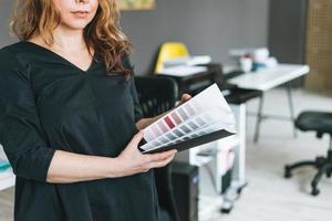 Encantadora mujer adulta sonriente de mediana edad con cabello rizado diseñadora arquitecta con paleta de colores en las manos en la oficina moderna foto