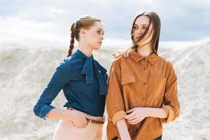 Fashion beauty portrait of young women sisters in brown organic velvet jeans shirts on desert background photo