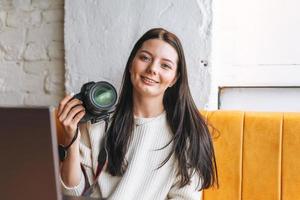 morena sonriente joven fotógrafa trabajando con su cámara y portátil en el café foto