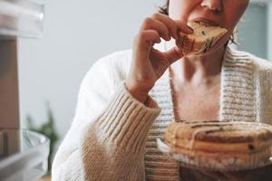 Attractive friendly brunette woman middle age in cozy cardigan eating cake from refrigerator at kitchen at home photo