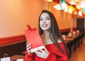 Beautiful young asian woman in red clothes with red gift bag in restaurant, celebrating Chinese New Year photo