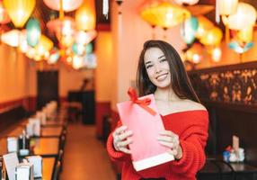 Beautiful young asian woman in red clothes with red gift bag in restaurant, celebrating Chinese New Year photo