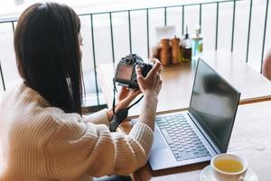 Brunette smiling young woman photographer working with her camera and laptop in cafe photo