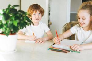 Two siblings brother and sister toddler boy tween girl drawing on table in kitchen at the home photo