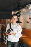 morena sonriente joven fotógrafa trabajando con su cámara en el café foto