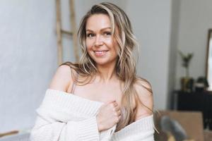 Blonde smiling woman 35 year clean fresh face and hands with long hair in cozy knitted cardigan at bright interior photo