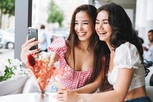 Happy brunette young girls friends in summer clothes take selfie on mobile phone in the summer street cafe photo