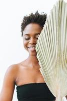 bella joven afroamericana sonriente con ojos cerrados modelo de moda de belleza con hoja seca sobre fondo blanco, concepto ecológico foto