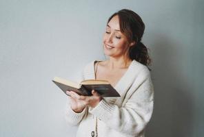 Atractiva y amable mujer morena sonriente de mediana edad leyendo un libro en casa vibraciones acogedoras temporada de frío foto