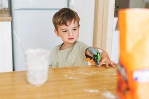 Toddler boy have fun while cooking with flour at the table in kitchen at home. Boy playing with the toy photo