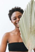 Hermosa mujer joven afroamericana sonriente belleza modelo de moda mirando a la cámara con hojas secas sobre fondo blanco, concepto ecológico belleza natural foto