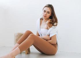 Young woman in white hoodie on shoulders beautiful fit girl in sport wear sitting on floor in the white studio photo