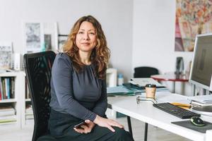 Encantadora mujer adulta sonriente de mediana edad con el pelo rizado arquitecto diseñador gerente que trabaja en una oficina moderna y luminosa foto