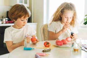 Two siblings brother and sister toddler boy tween girl painting easter eggs on kitchen at home on spring sunny day photo