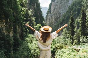 una joven viajera con el pelo largo y rubio con sombrero de paja mira la hermosa vista de las montañas, la gente por detrás foto