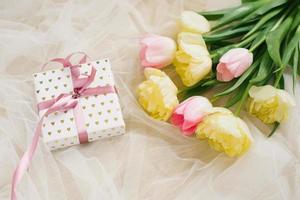 Beautiful spring bouquet of pink and yellow tulips and a gift with a ribbon on a beige background. Flat lay and copy space photo