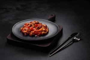 Delicious juicy meat with hot peppers and sauce on a black ceramic plate photo