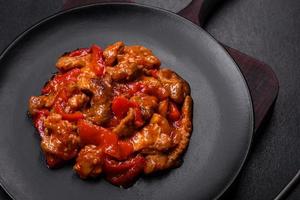 Delicious juicy meat with hot peppers and sauce on a black ceramic plate photo