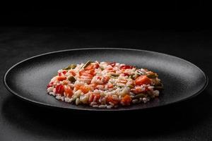 Delicious fresh risotto with vegetables, spices and herbs on a black plate photo