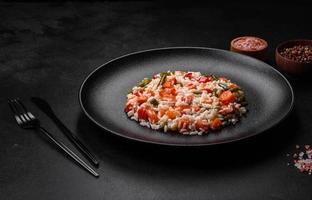 Delicious fresh risotto with vegetables, spices and herbs on a black plate photo