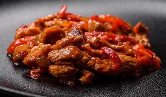 Delicious juicy meat with hot peppers and sauce on a black ceramic plate photo