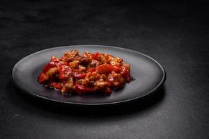 Delicious juicy meat with hot peppers and sauce on a black ceramic plate photo