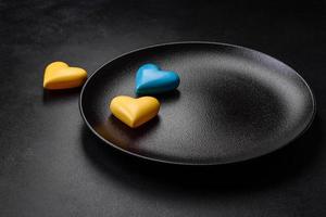 corazones de chocolate con los colores de la bandera ucraniana en un plato de cerámica negra foto