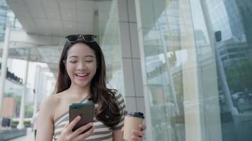 retrato de moda de estilo de vida femenino asiático feliz moderno. bella y atractiva joven disfruta de un paseo elegante con paquetes de bolsas de compras usa un smartphone en la calle, ropa de moda en un centro comercial video