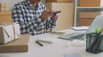 los hombres están tomando fotografías de los productos y enviándoselos a los clientes cuando hacen pedidos en línea. los hombres están cargando fotos de teléfonos móviles en el sitio web para la venta en línea. ideas de tendencias comerciales en línea. video