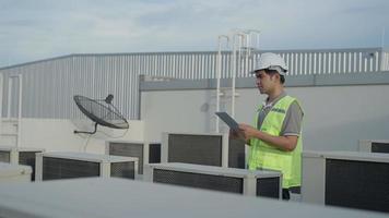 ingeniero de mantenimiento asiático trabaja en el techo de la fábrica. supervisor de inspección y verificación del sistema de compresores y planes de instalación de sistemas de aire acondicionado en obras de construcción de edificios modernos. video